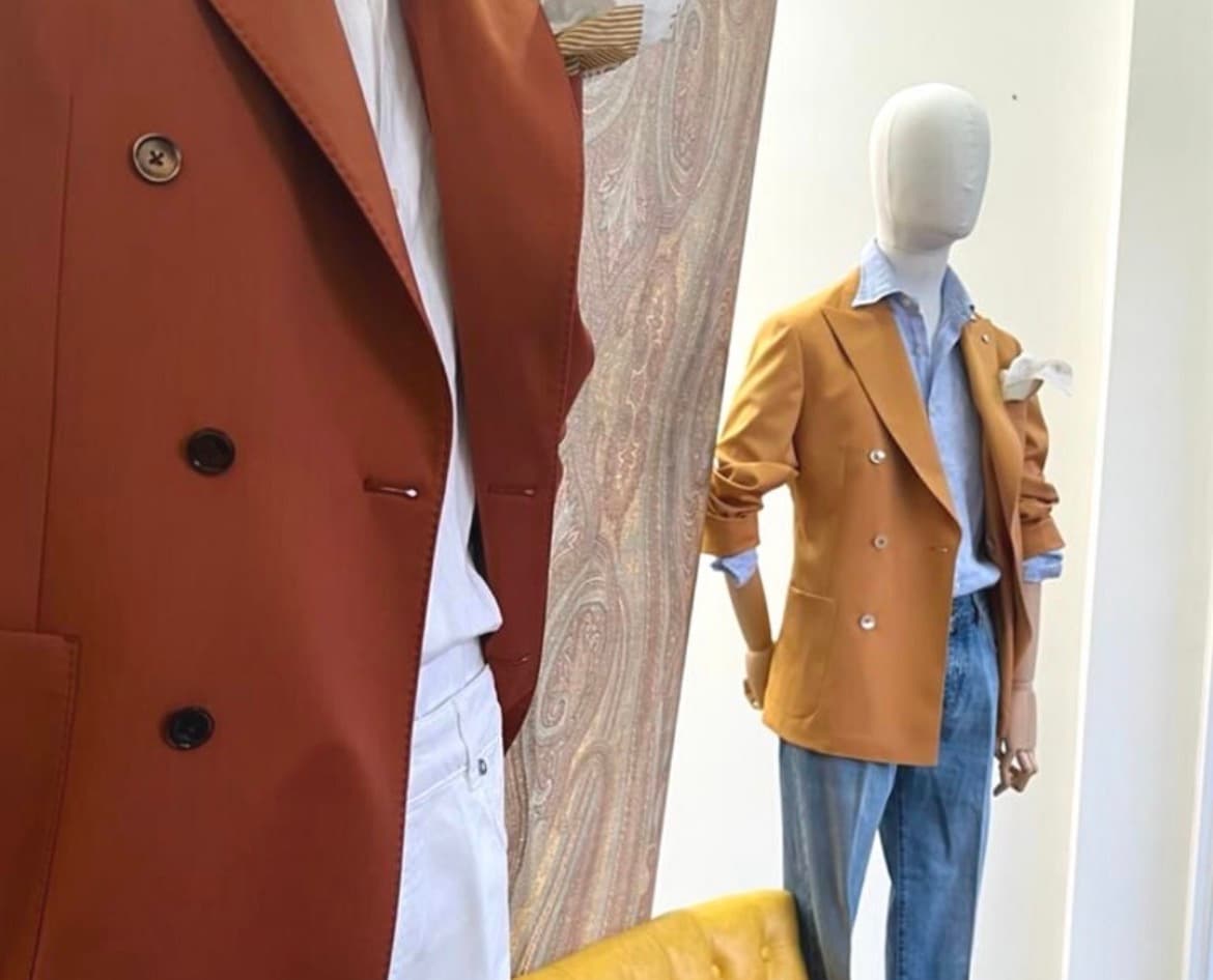 Capi sartoriali esposti in showroom: giacca doppiopetto e manichino con blazer e denim
