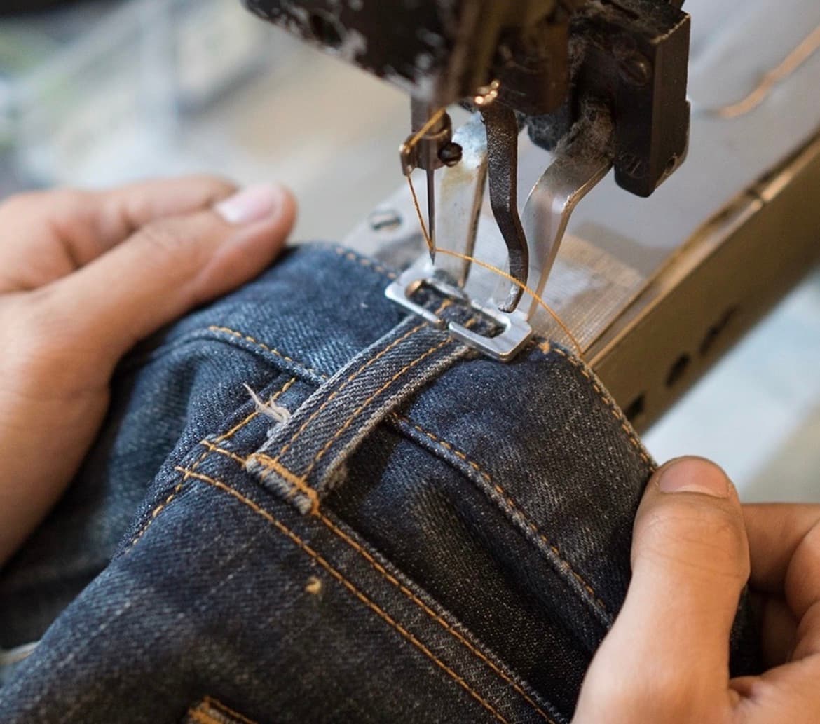 Mani al lavoro sulla cucitura di un capo alla macchina industriale